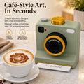 A retro-style instant coffee art printer in sage green and gold sits on a marble countertop next to a cup of cappuccino with a frosted latte art design. The product features a vintage camera design with a pull-out tray displaying 'Cupcake' and is shown with promotional text on the left.