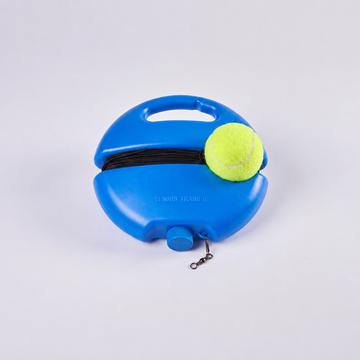 A blue tennis ball retriever tool with a handle, black elastic band, and a yellow tennis ball resting on top, photographed on a light gray studio background.